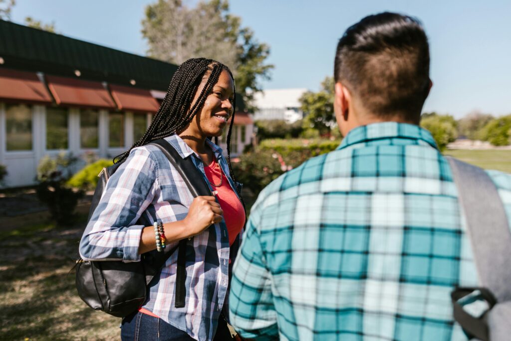 Young adults engaged in a joyful conversation outside a college building, showcasing friendship and diversity.
